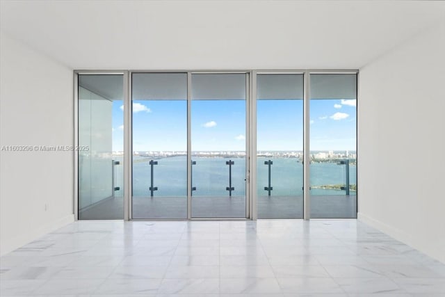 unfurnished room featuring a water view, expansive windows, and baseboards