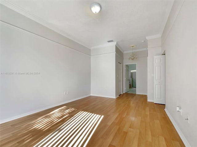 unfurnished room with an inviting chandelier, ornamental molding, and light hardwood / wood-style flooring