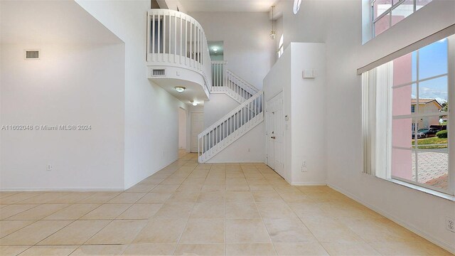 hall with light tile patterned flooring, a wealth of natural light, and a high ceiling