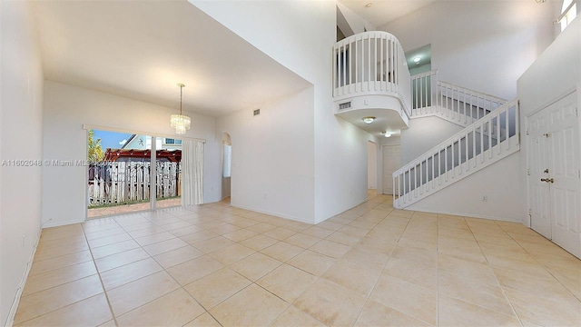 empty room featuring a towering ceiling, a notable chandelier, and light tile patterned floors