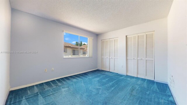 unfurnished bedroom with two closets, carpet, and a textured ceiling