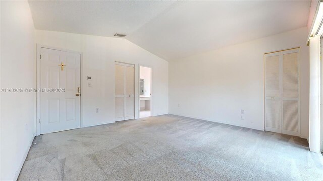 unfurnished bedroom with light carpet, multiple closets, and lofted ceiling