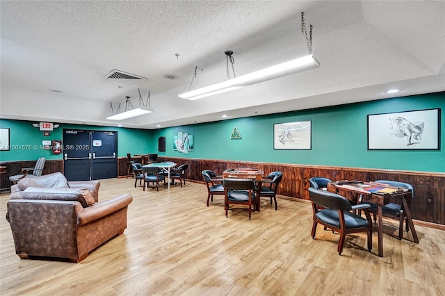 game room featuring a textured ceiling, light hardwood / wood-style flooring, and wood walls