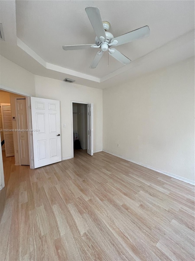 unfurnished bedroom with ceiling fan, a tray ceiling, and light wood-type flooring