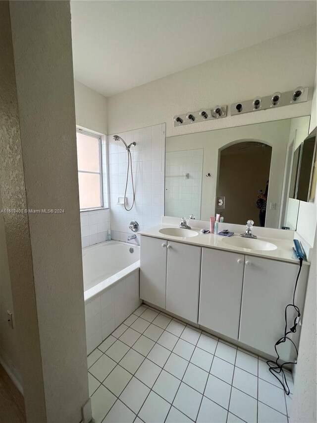 bathroom featuring tile floors, a relaxing tiled bath, vanity with extensive cabinet space, and dual sinks