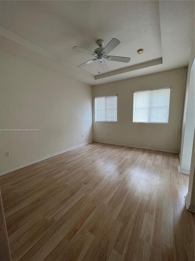 unfurnished room featuring wood-type flooring, ceiling fan, and a tray ceiling