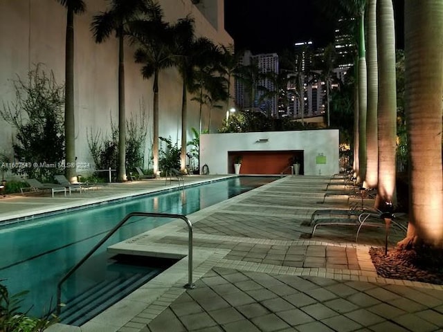 pool at night featuring a patio area