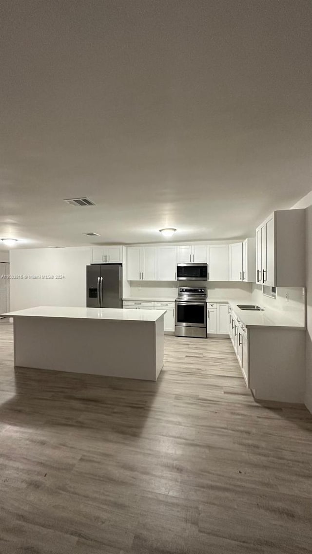 kitchen with sink, light wood-type flooring, a kitchen island, white cabinetry, and stainless steel appliances