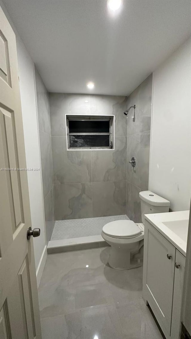 bathroom featuring a tile shower, vanity, and toilet