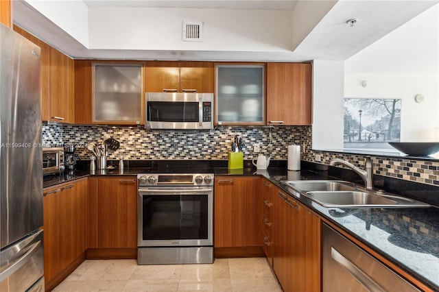 kitchen featuring sink, appliances with stainless steel finishes, dark stone counters, and decorative backsplash