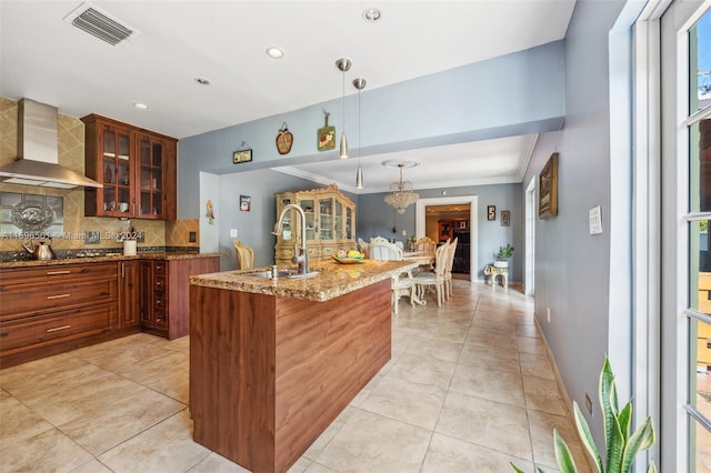 kitchen with sink, ornamental molding, pendant lighting, wall chimney range hood, and backsplash