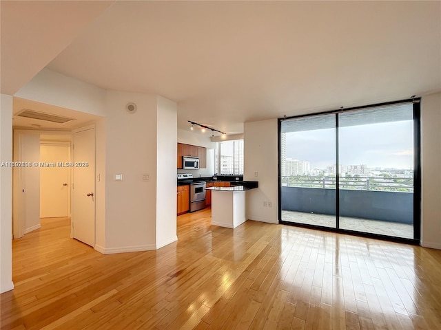 unfurnished living room featuring track lighting, light wood-type flooring, a healthy amount of sunlight, and floor to ceiling windows