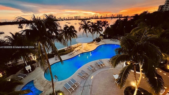 pool at dusk featuring a patio and a water view