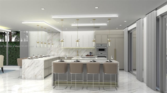 kitchen with white cabinetry, double oven, a center island with sink, a kitchen bar, and decorative backsplash