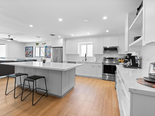 kitchen featuring a breakfast bar, a center island, light hardwood / wood-style flooring, appliances with stainless steel finishes, and ceiling fan