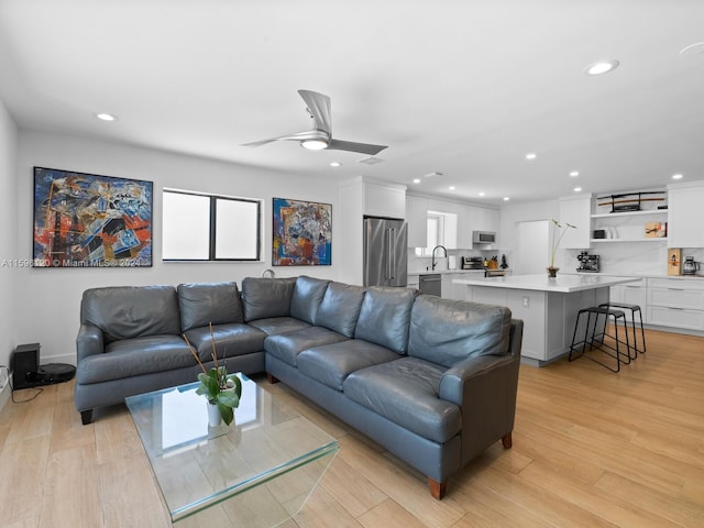 living room with light wood-type flooring, sink, and ceiling fan