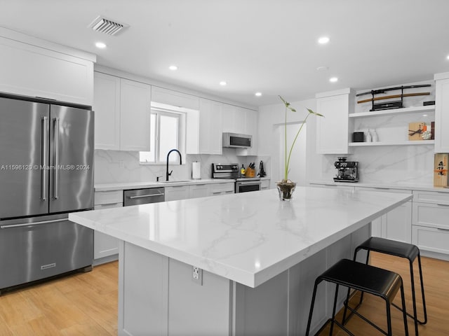 kitchen with stainless steel appliances, white cabinets, a kitchen island, and light wood-type flooring