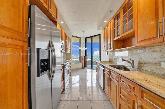 kitchen with sink, light tile patterned floors, stainless steel appliances, light stone counters, and decorative backsplash