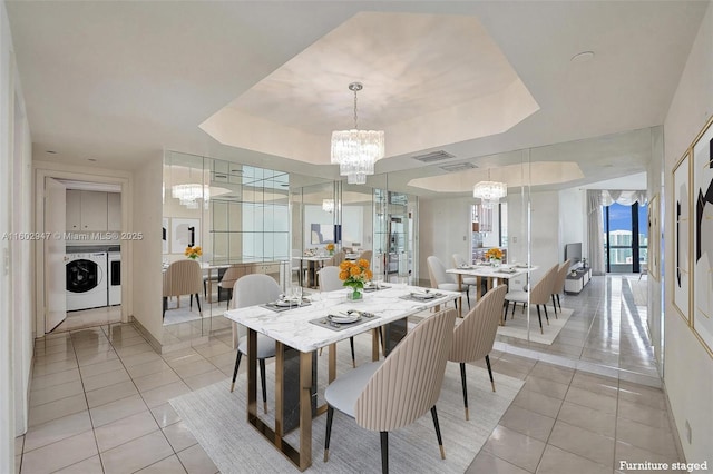 dining space featuring light tile patterned floors, a tray ceiling, washer and clothes dryer, and a chandelier