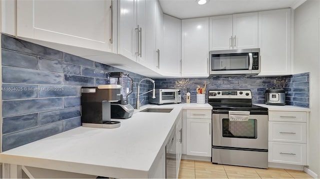 kitchen with light tile patterned flooring, decorative backsplash, sink, stainless steel appliances, and white cabinets