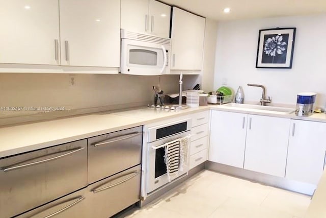 kitchen with light tile patterned floors, sink, white cabinetry, and oven