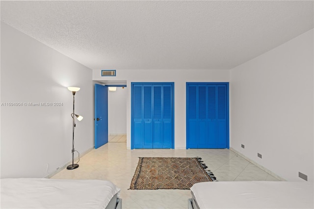 bedroom with two closets, a textured ceiling, and light tile floors