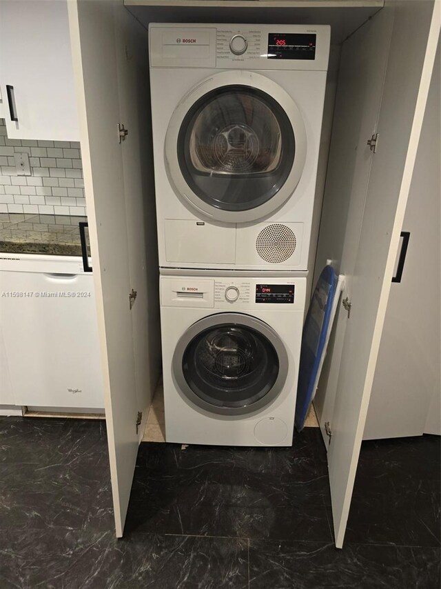 laundry room with stacked washer and dryer and dark tile flooring