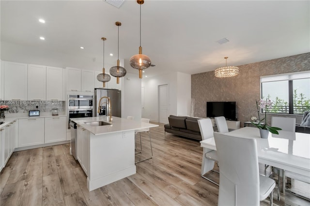 kitchen featuring light hardwood / wood-style floors, stainless steel appliances, an island with sink, and white cabinets