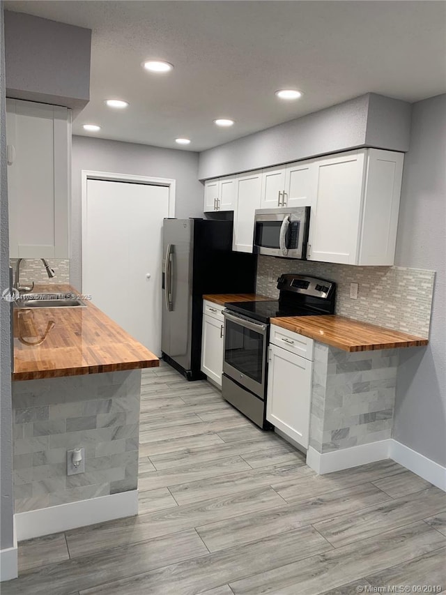 kitchen featuring butcher block counters, sink, white cabinetry, stainless steel appliances, and backsplash