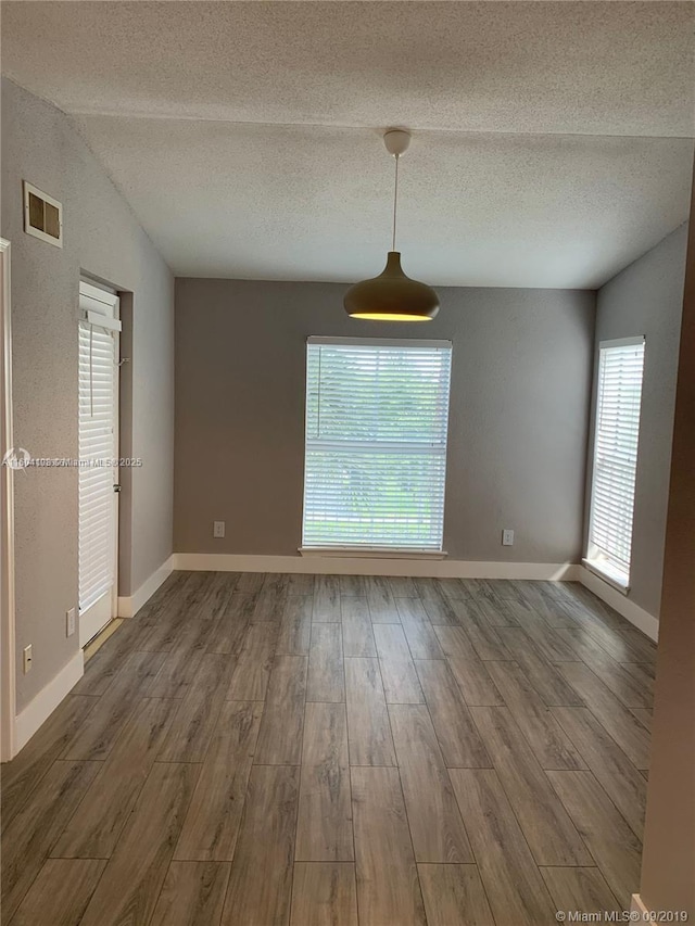 unfurnished room featuring hardwood / wood-style flooring, lofted ceiling, and a textured ceiling