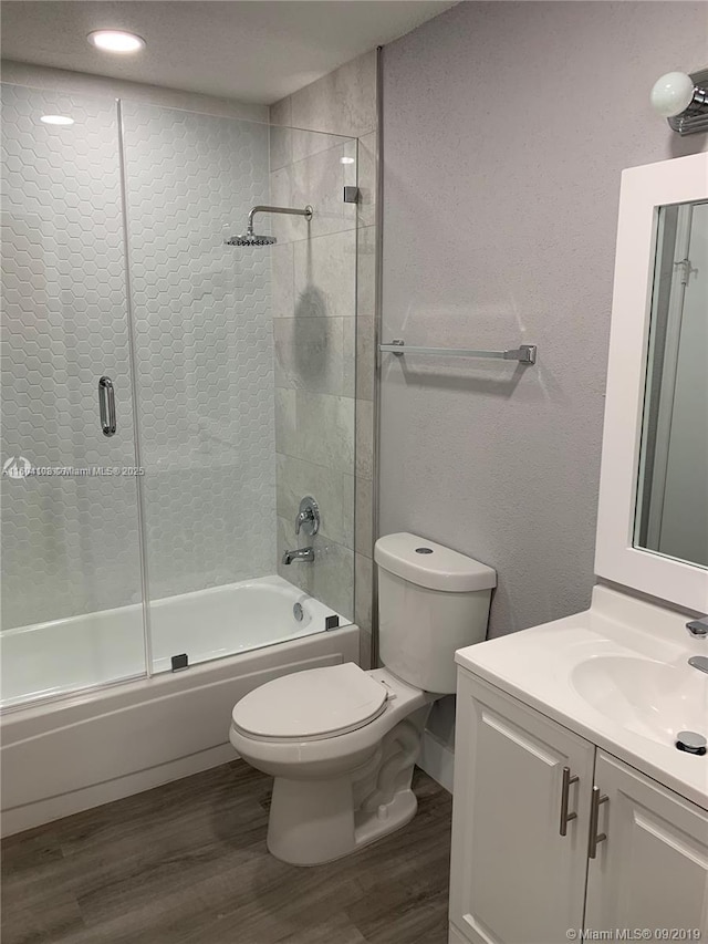 full bathroom with hardwood / wood-style flooring, vanity, shower / bath combination with glass door, and toilet