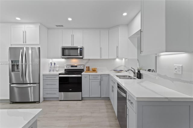 kitchen with white cabinets, light hardwood / wood-style floors, light stone counters, sink, and stainless steel appliances