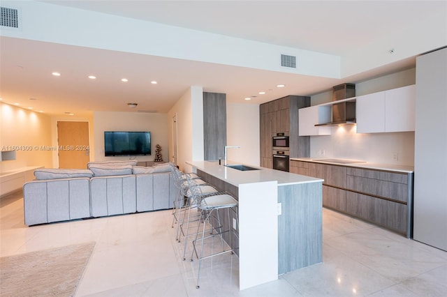 kitchen featuring a kitchen breakfast bar, wall chimney range hood, sink, white cabinets, and electric cooktop