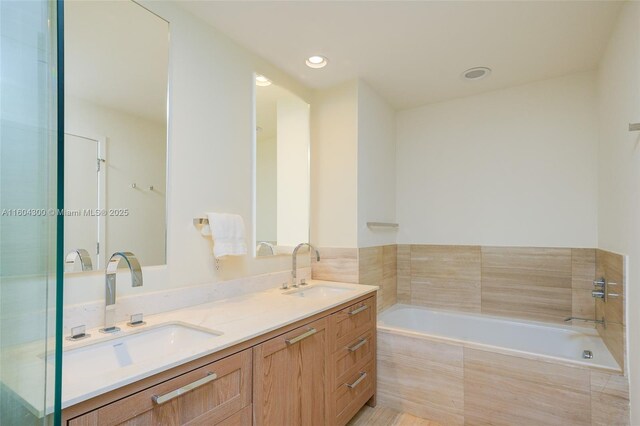 bathroom with dual vanity and tiled bath