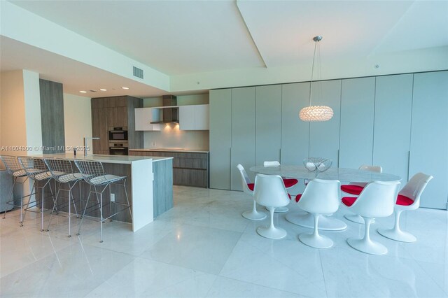 kitchen with decorative light fixtures, a kitchen breakfast bar, wall chimney exhaust hood, and light tile floors