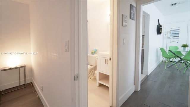 hall with dark wood-type flooring, visible vents, and baseboards