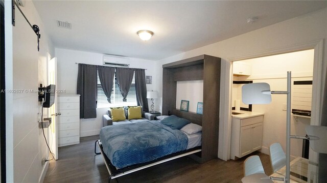 bedroom featuring a barn door, dark wood-type flooring, and a wall mounted air conditioner