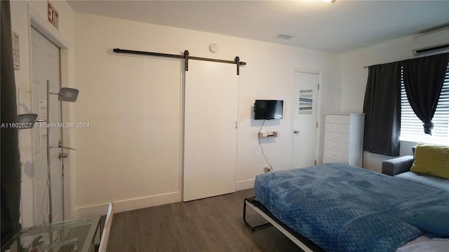 bedroom featuring dark wood-style floors, an AC wall unit, visible vents, and a barn door