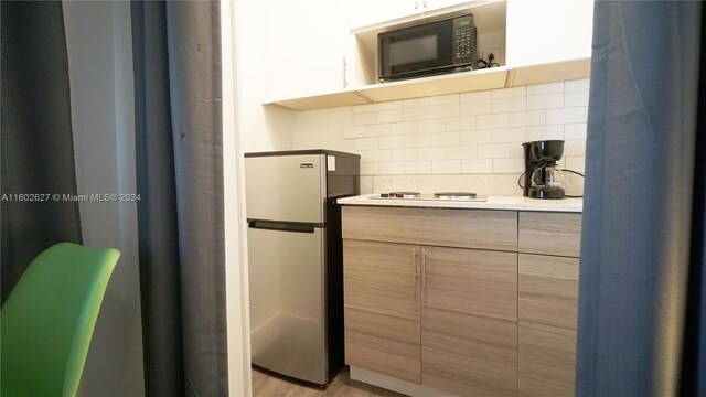 kitchen featuring light hardwood / wood-style flooring, tasteful backsplash, black microwave, stainless steel fridge, and white gas stovetop