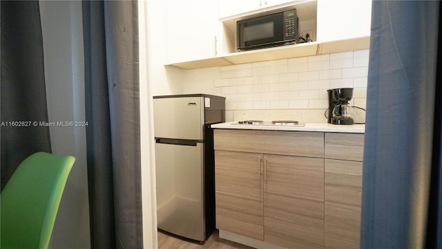 kitchen with black microwave, light countertops, freestanding refrigerator, tasteful backsplash, and modern cabinets