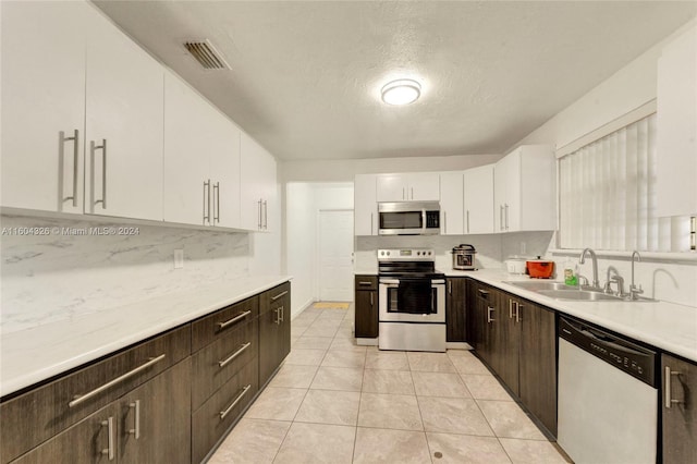 kitchen featuring sink, white cabinetry, backsplash, dark brown cabinets, and stainless steel appliances