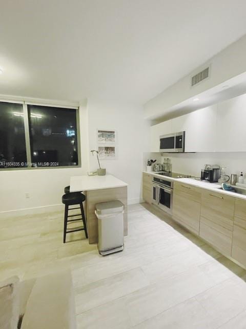 kitchen with a breakfast bar area, light brown cabinetry, and appliances with stainless steel finishes