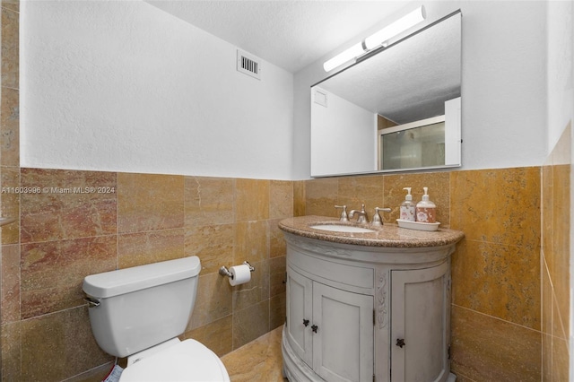 bathroom featuring vanity, a shower with shower door, tile walls, and toilet