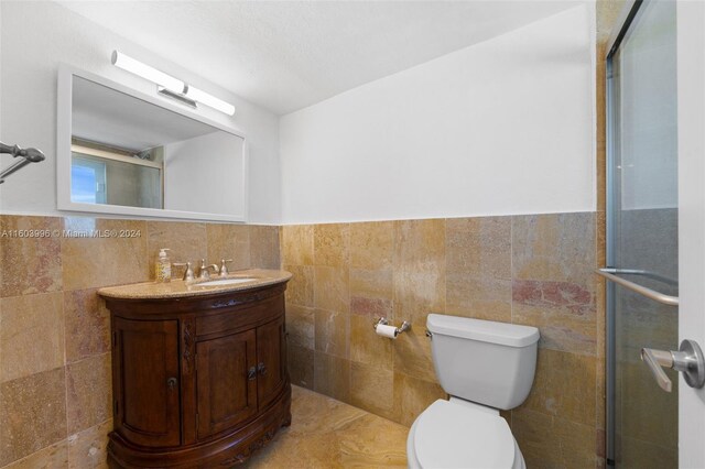 bathroom featuring vanity, a shower with door, tile walls, and toilet