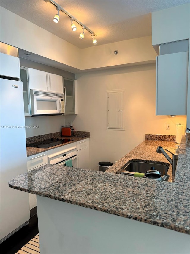 kitchen with dark stone counters, kitchen peninsula, rail lighting, sink, and white appliances