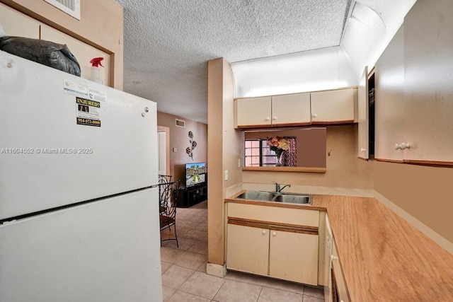 kitchen featuring cream cabinetry, light tile patterned floors, white refrigerator, and sink