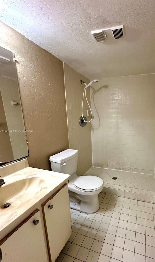 bathroom with vanity, tile patterned floors, toilet, tiled shower, and a textured ceiling