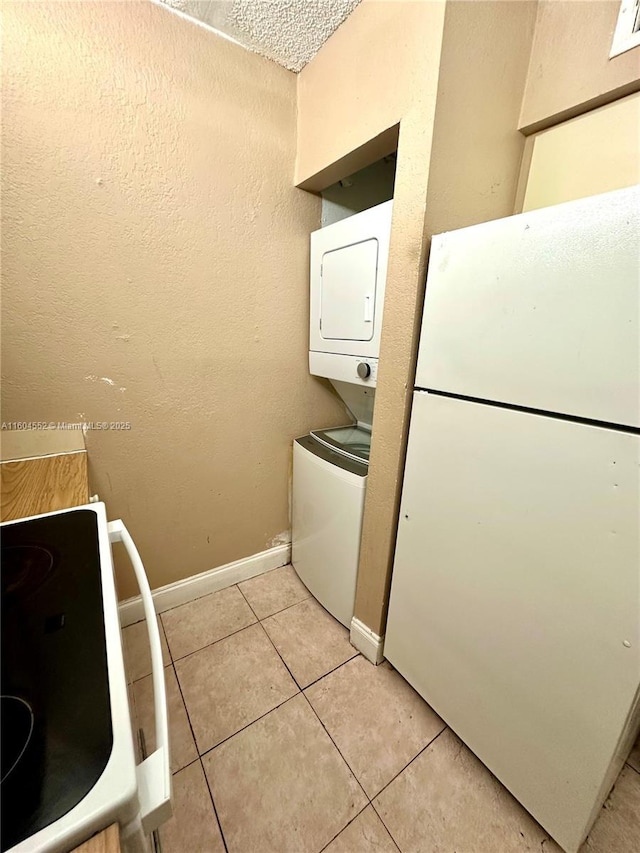 washroom featuring a textured ceiling, light tile patterned flooring, and stacked washer and dryer