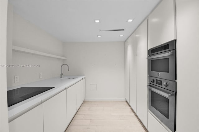 kitchen with black electric cooktop, white cabinets, sink, stainless steel double oven, and light hardwood / wood-style flooring