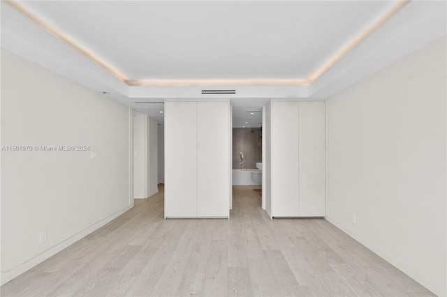 unfurnished bedroom with ensuite bathroom, light hardwood / wood-style flooring, and a raised ceiling